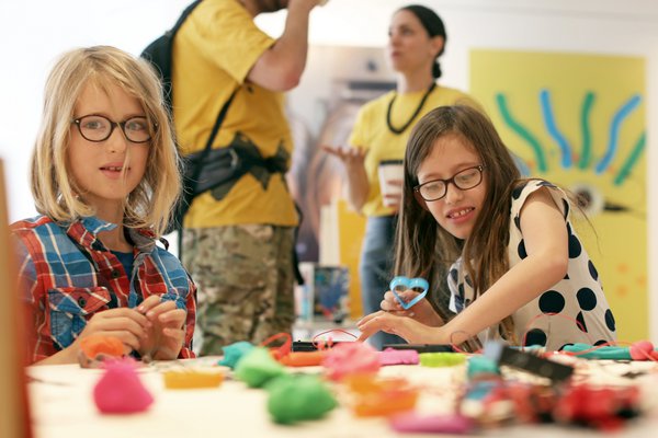  Two young girls wearing glasses are crafting shapes out of play-doh