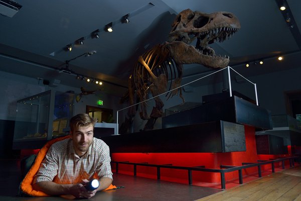  A man with a torch and sleeping bag poses in front of the replica T. rex skeleton at the Great North Museum